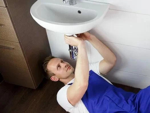 Ein Mann in blauen Overalls repariert ein Waschbecken.