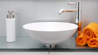 Ein Badezimmerwaschbecken mit einer weissen Schüssel und orangefarbenen Handtüchern.